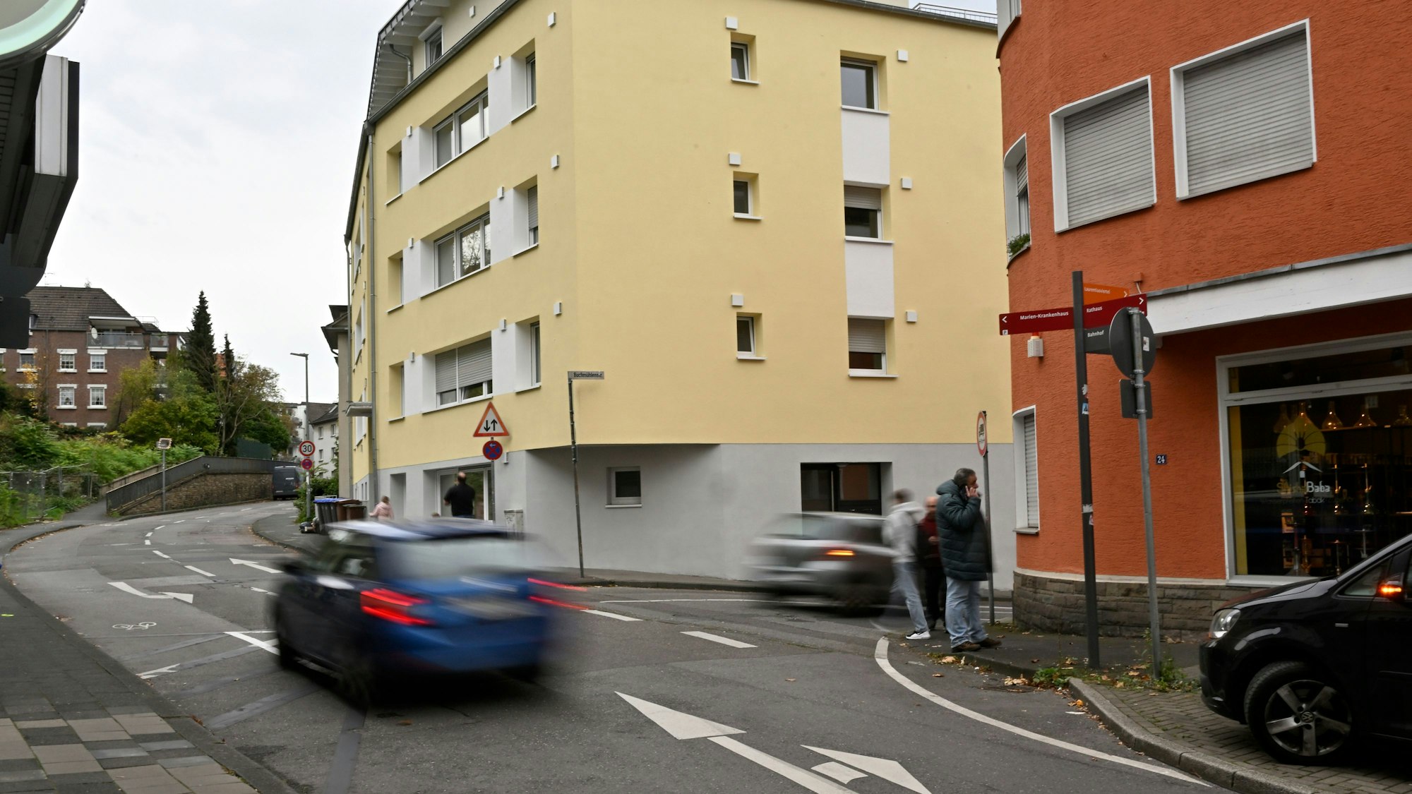 Ein blaues Auto fährt auf der Laurentiusstraße, auf dem Bürgersteig stehen Passanten.