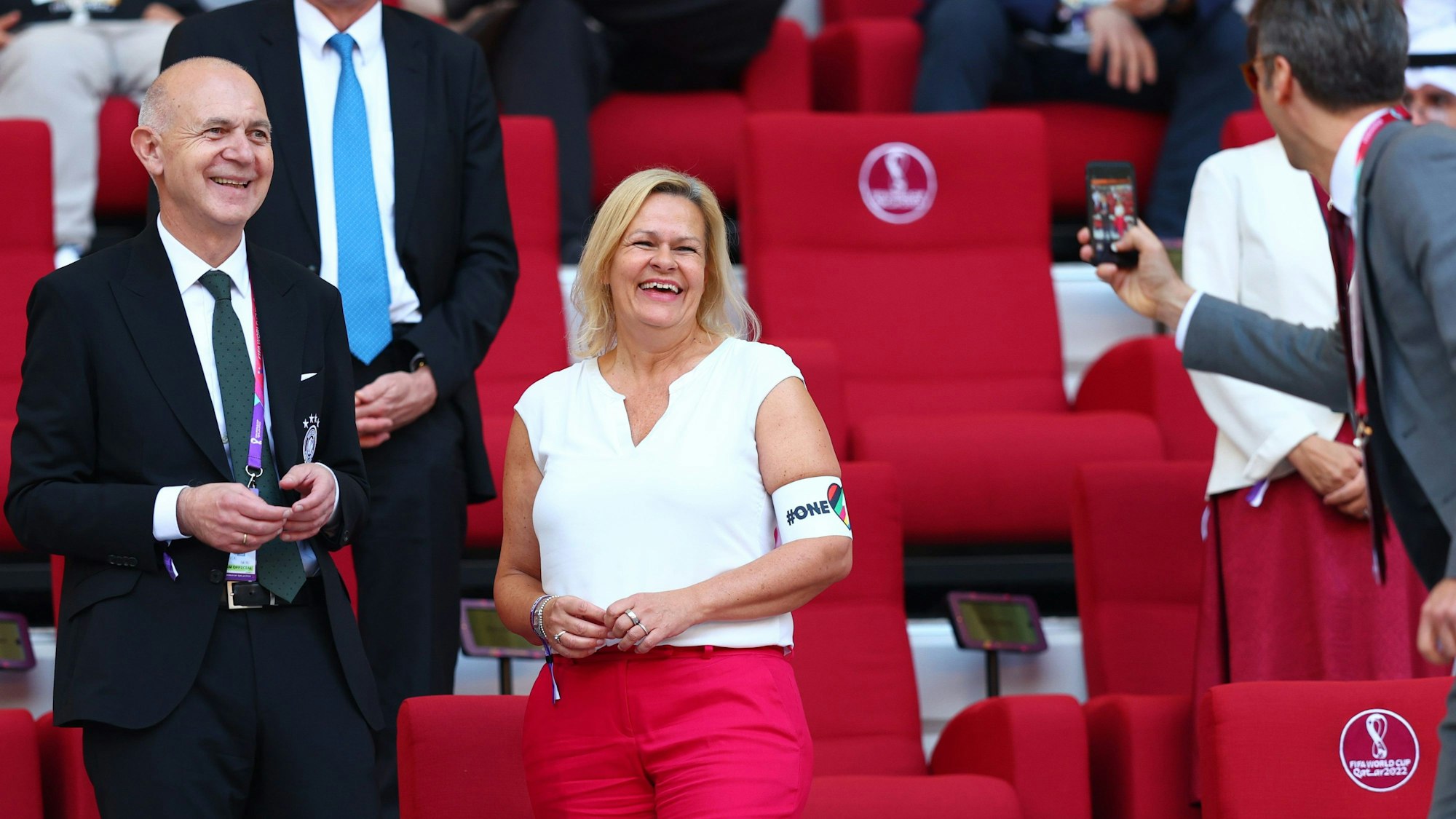 Bundesinnenministerin Nancy Faeser (SPD) und DFB-Präsident Bernd Neuendorf stehen auf der Tribüne bei der Fußball-WM in Katar und werden von einem Mann fotografiert. Faeser trägt die One-Love-Armbinde, die die Fifa kurz zuvor für Spieler untersagt hatte.