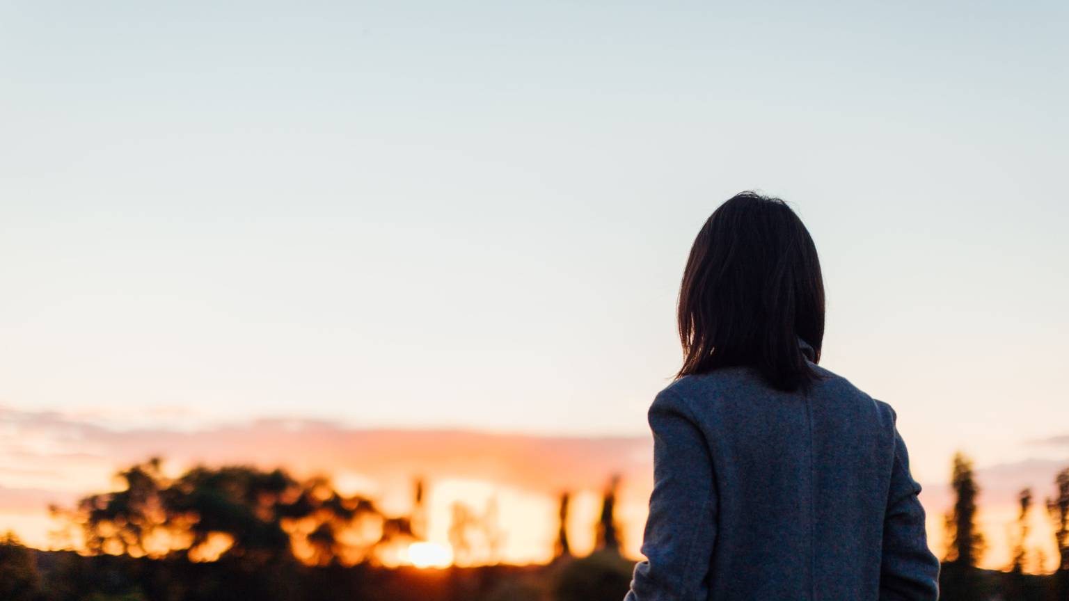 Frau von hinten blickt in einen Sonnenuntergang Foto: Getty Images / Oscar Wong