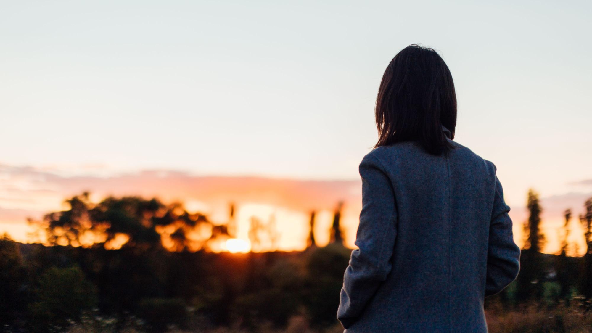 Frau von hinten blickt in einen Sonnenuntergang Foto: Getty Images / Oscar Wong