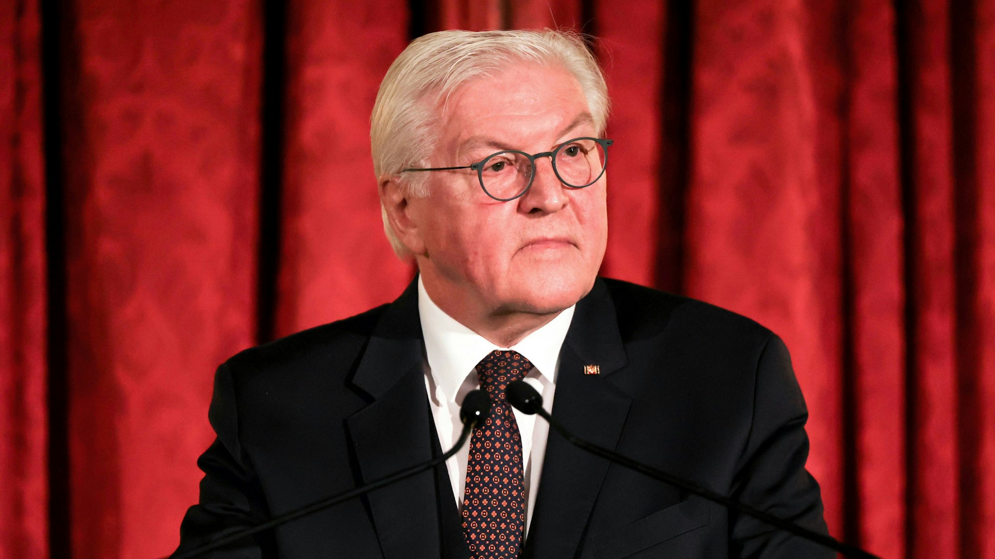 Bundespräsident Frank-Walter Steinmeier spricht nach der Verleihung des Henry-Kissinger-Preises 2022. Er steht vor einem roten Vorhang und guckt ernst an der Kamera vorbei.