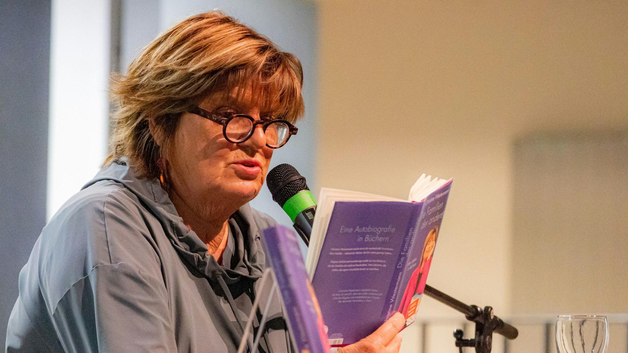 Christine Westermann sitzt auf einer Bühne im Bornheimer Gymnasium und liest aus ihrem neuen Buch.