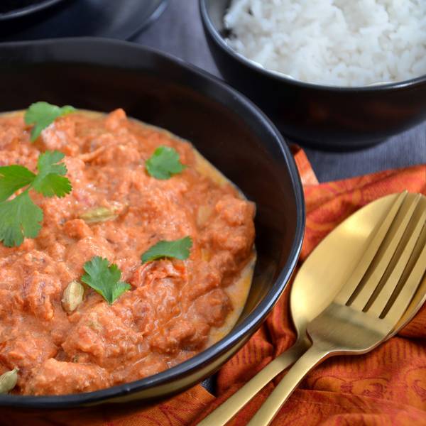 Ein indisches Hähnchen-Curry steht in einer Schüssel auf dem Tisch, mit Koriander bestreut.