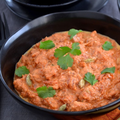 Ein indisches Hähnchen-Curry steht in einer Schüssel auf dem Tisch, mit Koriander bestreut.