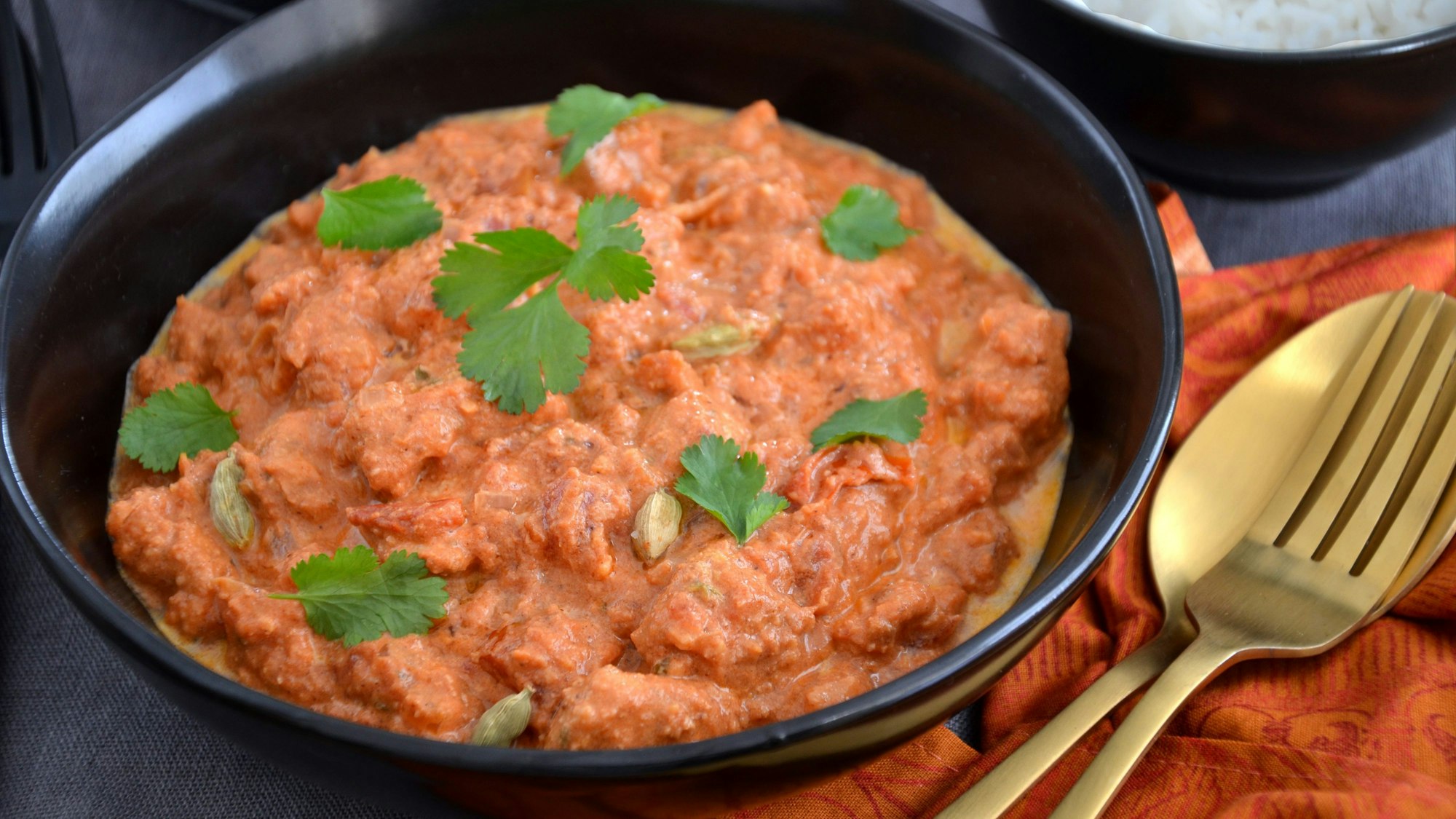 Ein indisches Hähnchen-Curry steht in einer Schüssel auf dem Tisch, mit Koriander bestreut.