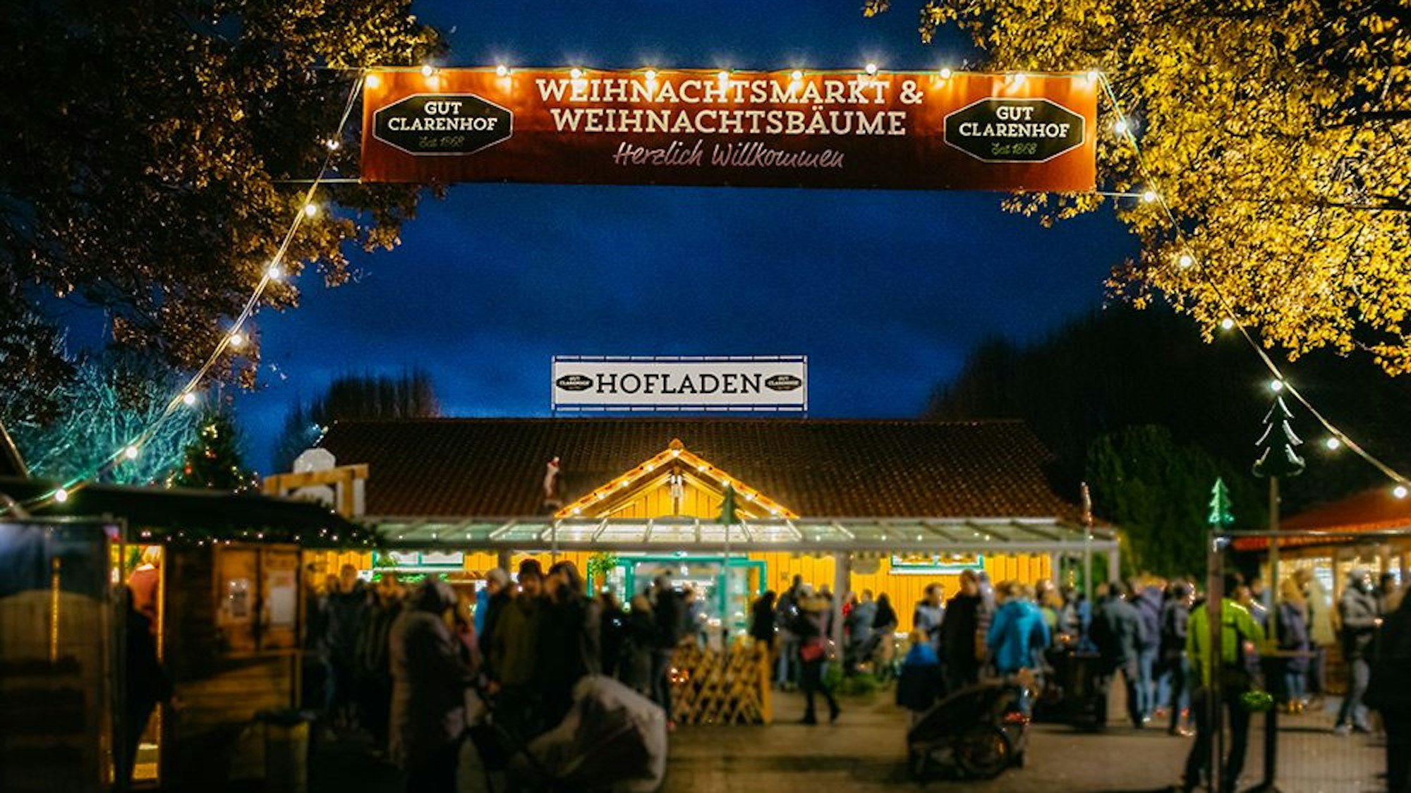 Beleuchteter Hofladen und Weihnachtsmarkt auf dem Gut Clarenhof in Köln Frechen bei Dunkelheit.