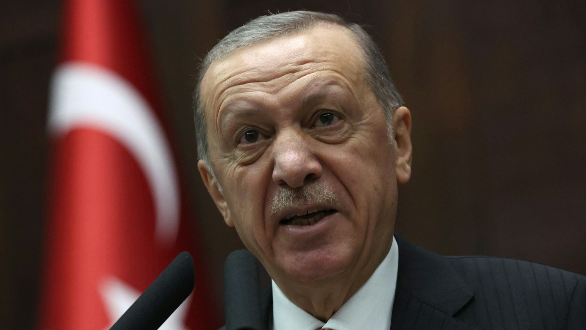 Der türkische Präsident Erdogan spricht in ein Mikrofon. Im Hintergrund ist die türkische Flagge.