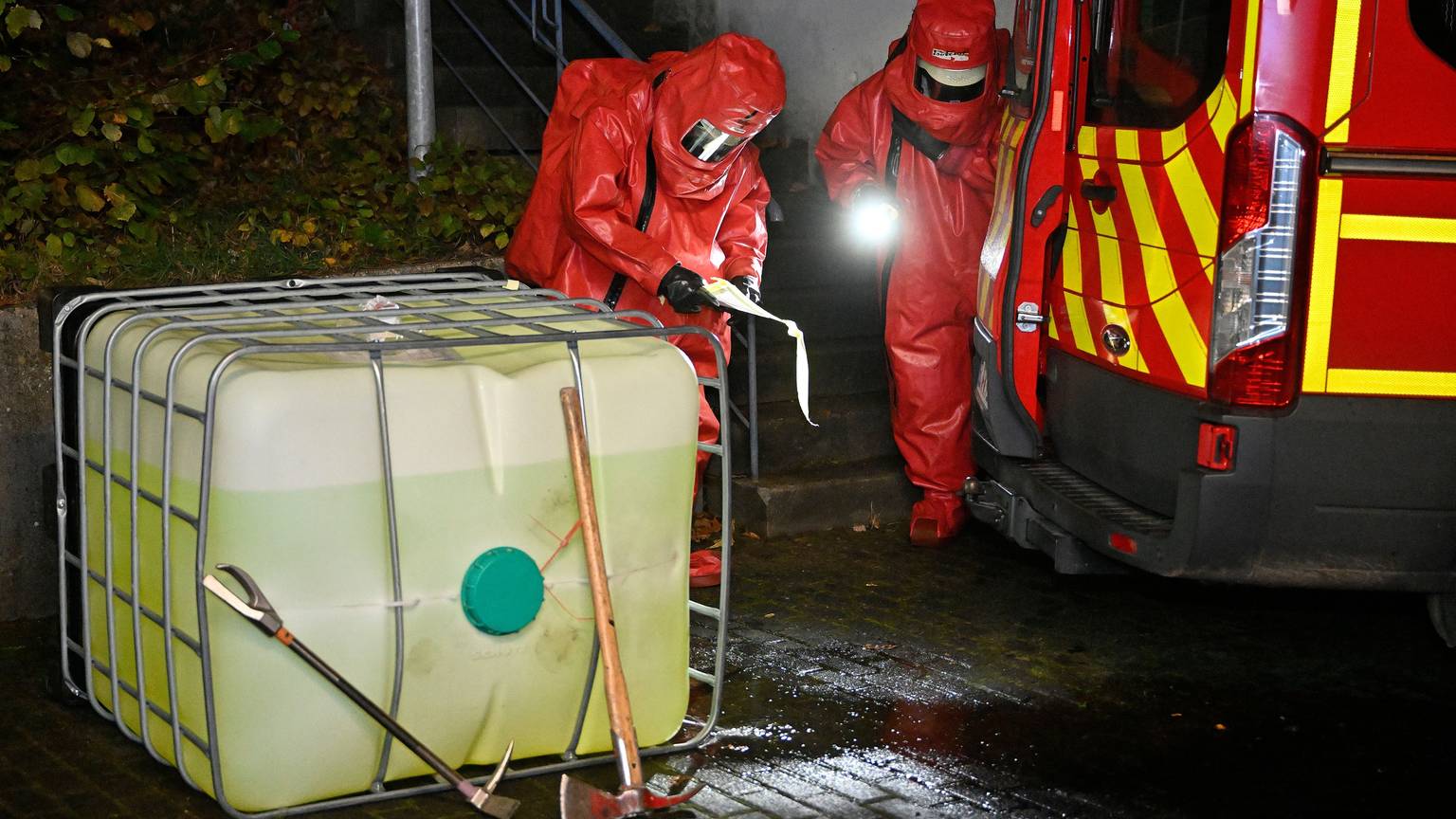 Feuerwehrleute in Chemikalienschutzanzügen untersuchen einen Kunststofftank.