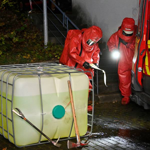 Feuerwehrleute in Chemikalienschutzanzügen untersuchen einen Kunststofftank.