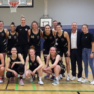 Die Basketballerinnen der Rheinland Lions in ihren schwarzen Trikots in einer Turnhalle.