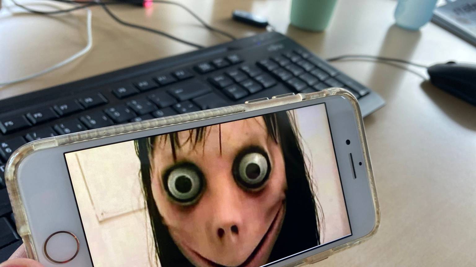 Ein Bild der Gruselfigur Momo ist auf einem Handy zu sehen.