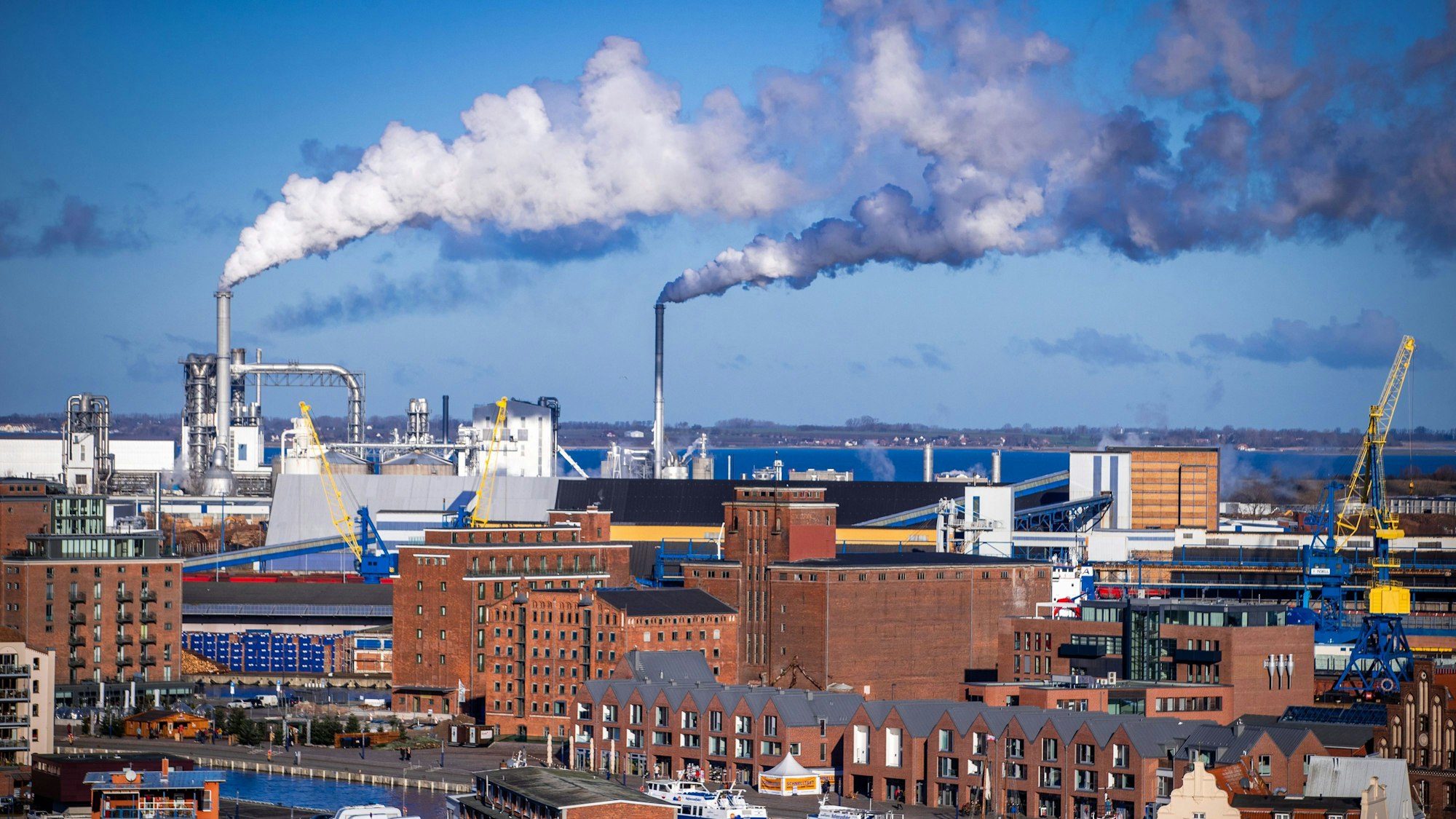 Rauch steigt aus Schornsteinen von holzverarbeitenden Industriebetrieben am Seehafen Wismar auf.