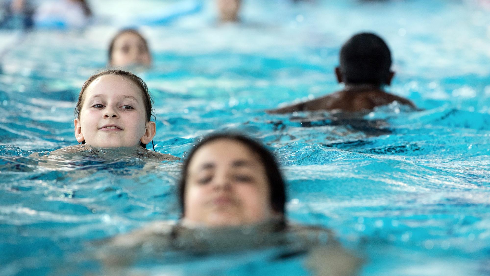 Mehrere Kinder schwimmen hintereinander im Wasser eines Hallenbads.