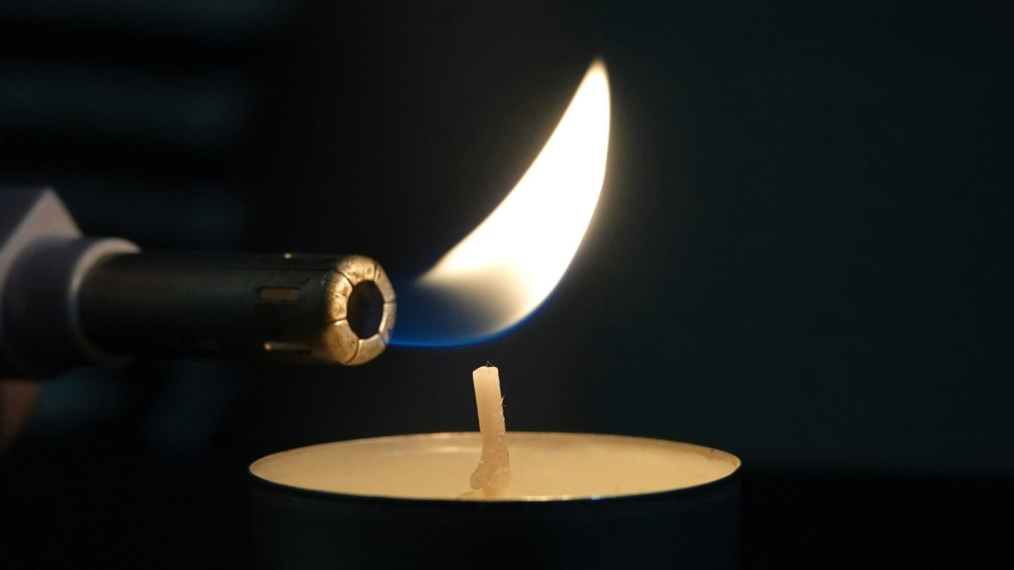 Die Flamme eines Feuerzeugs steht kurz davor einen Kerzendocht zu entzünden.