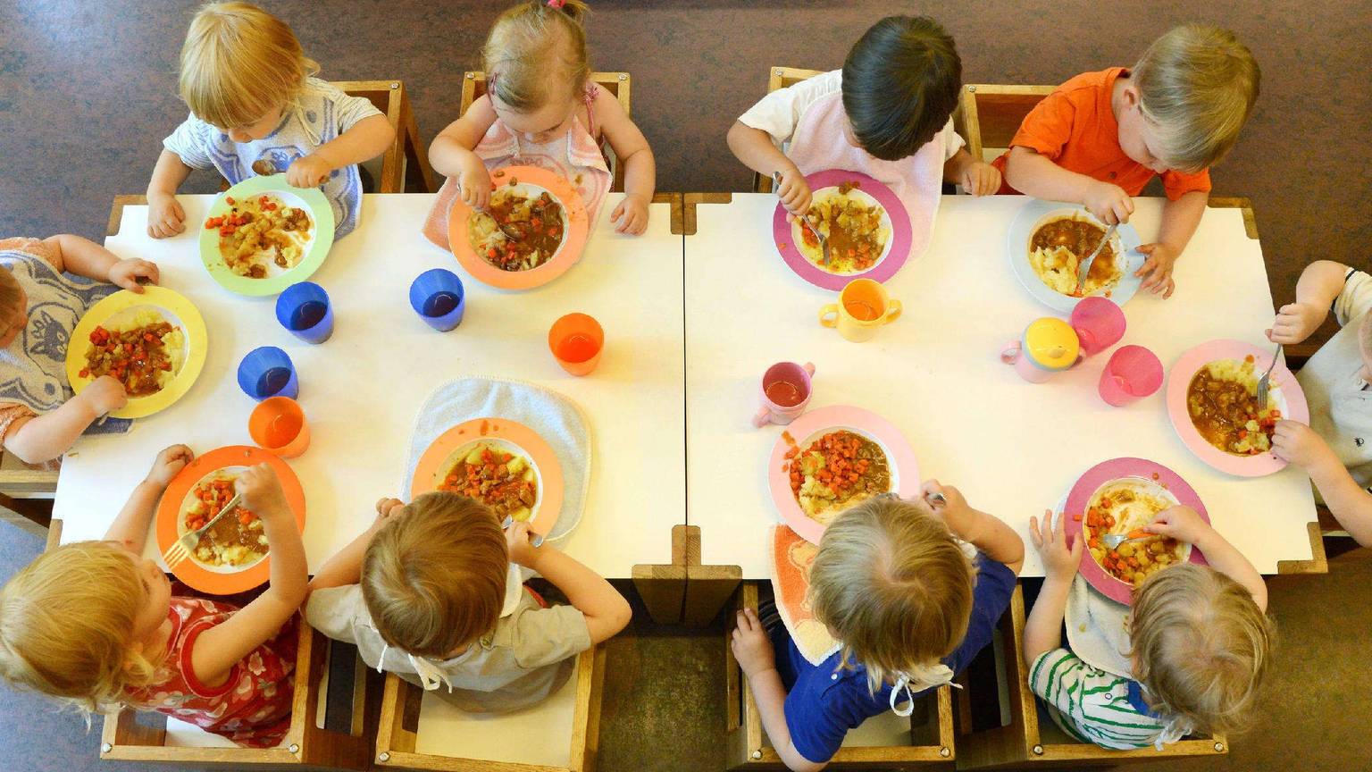 Kinder sitzen beim Mittagessen in einer Kindertageseinrichtung um einen Tisch.