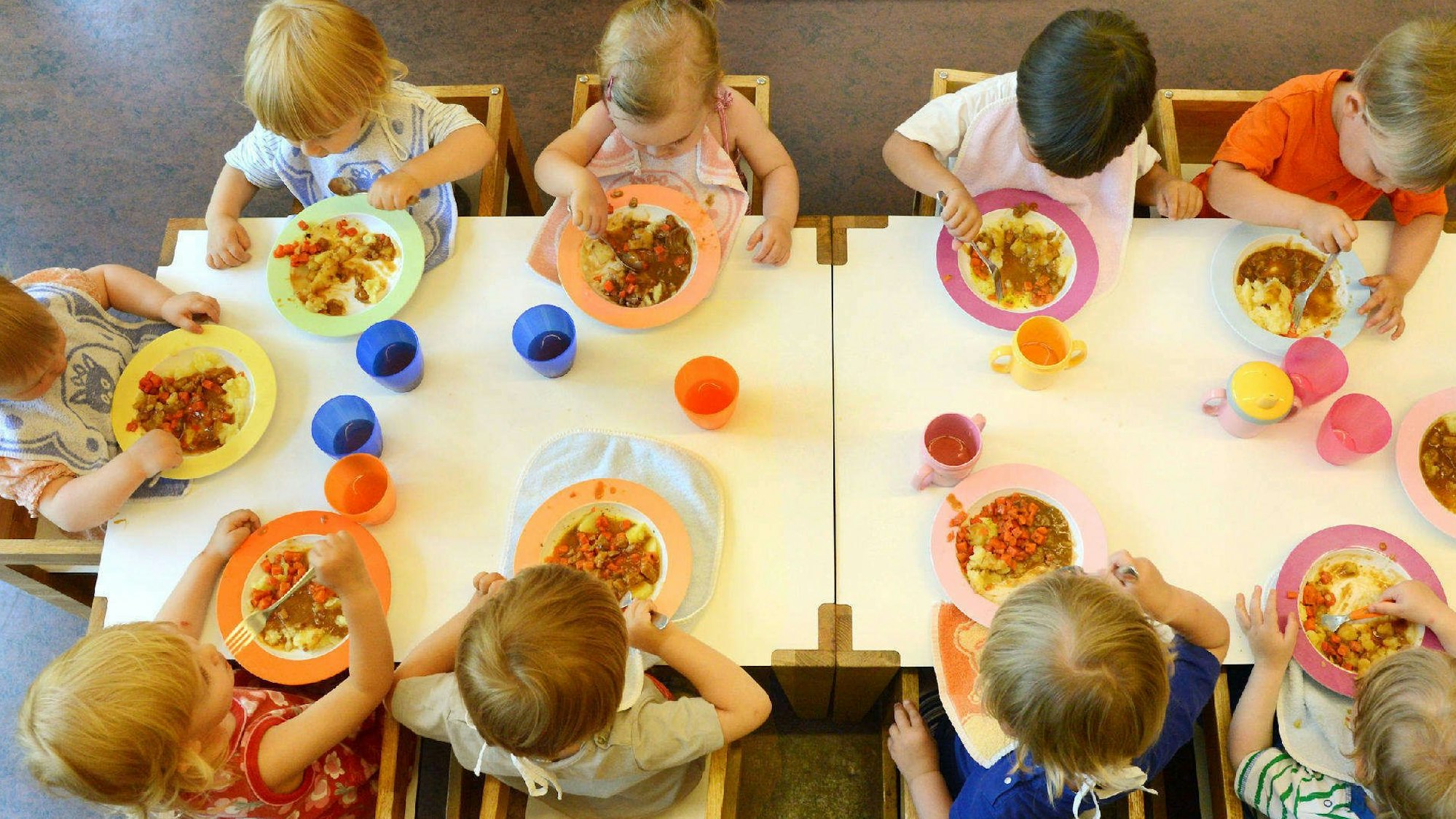 Kinder sitzen in einer Kindertageseinrichtung beim Mittagessen.