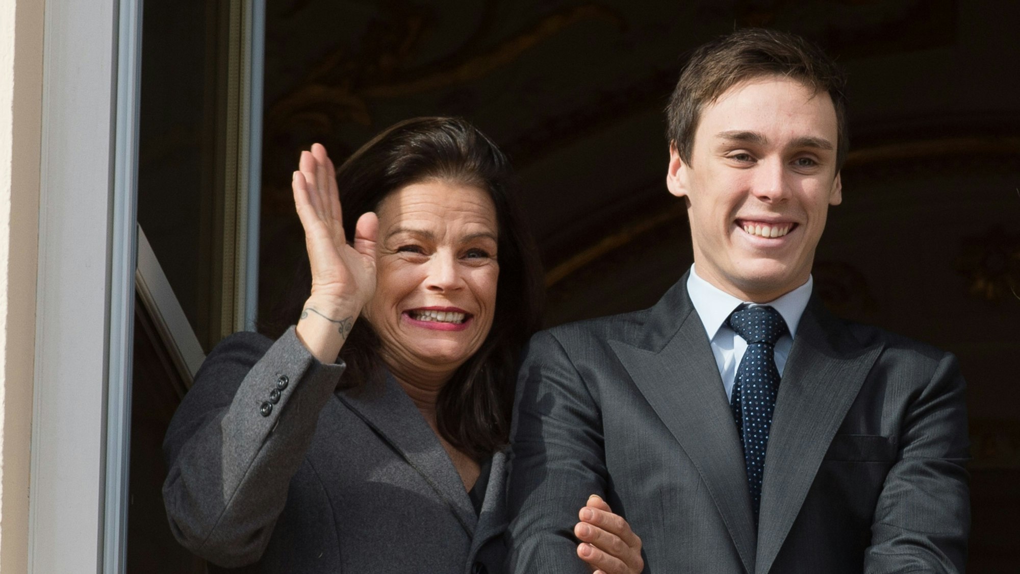 Prinzessin Stéphanie (l.) und Louis Ducruet (r.) auf dem Balkon des Fürstenpalasts. Sie winkt und hält seinen Arm, beide grinsen.