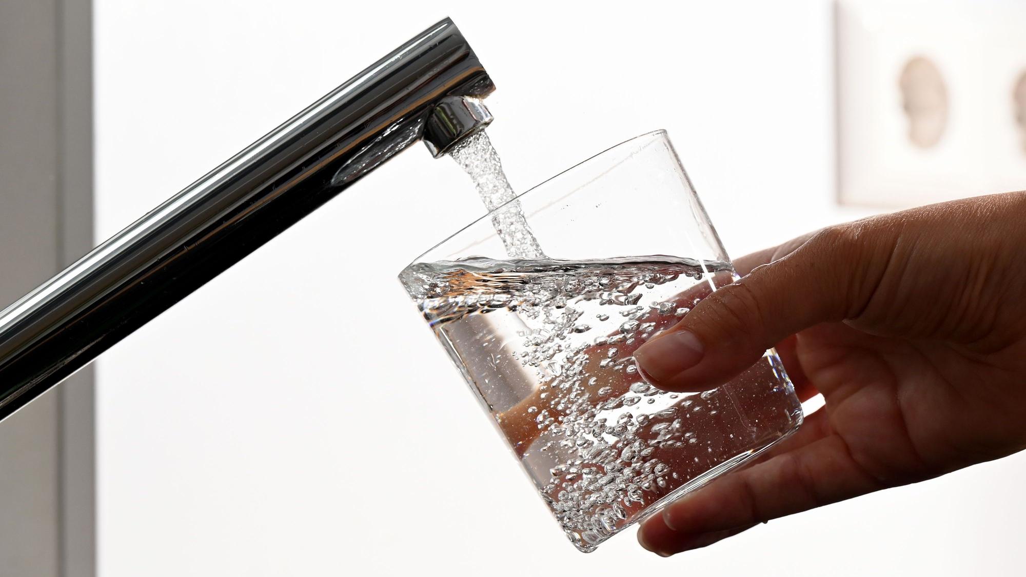 Eine Hand hält ein Wasserglas unter einen Wasserhahn.