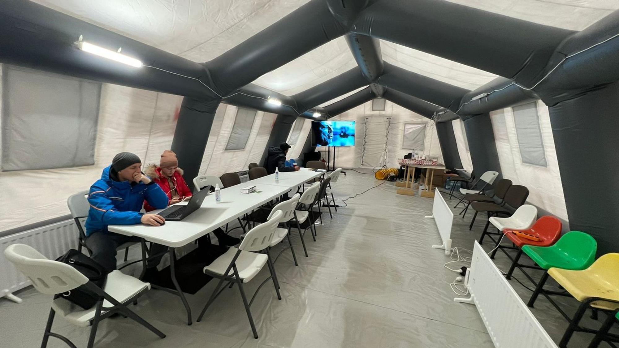 Zwei Bürger sitzen in einem beheizten Zelt in Butscha. Nur dort gibt es nach den russischen Angriffen Strom und Internet.