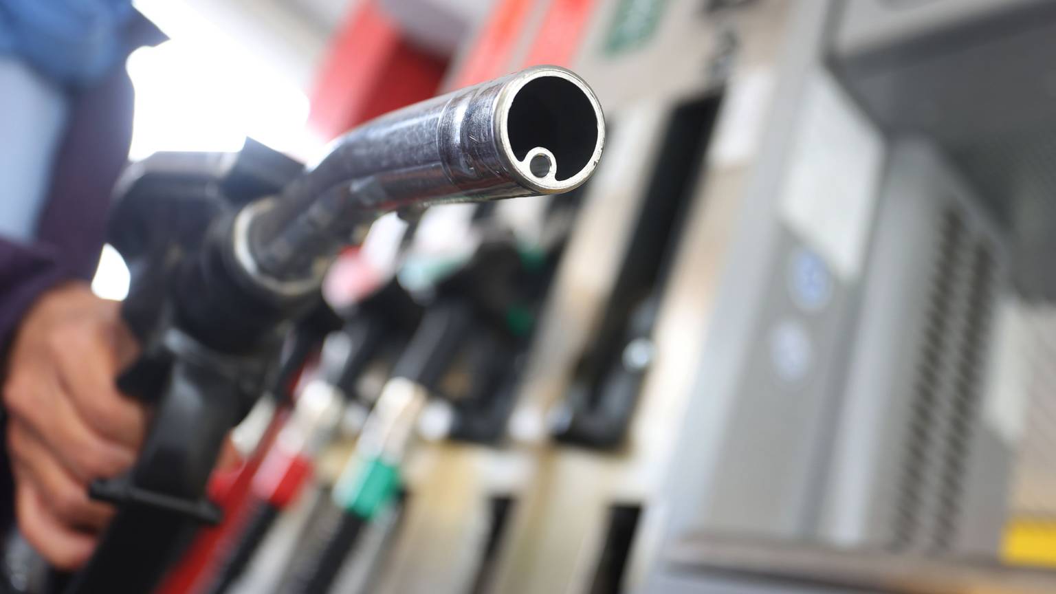 Eine Hand hält eine Zapfpistole auf einer Tankstelle.