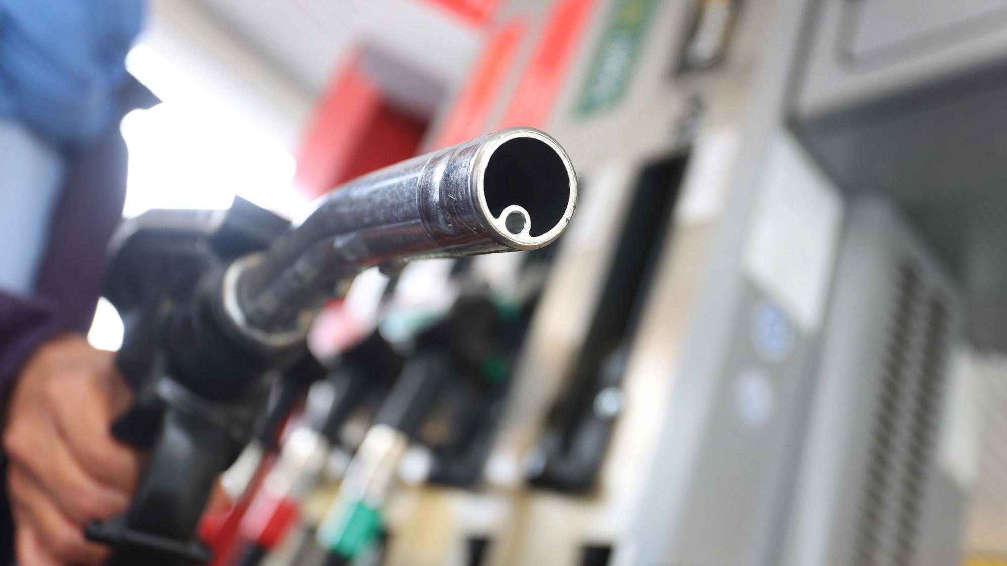Eine Hand hält eine Zapfpistole auf einer Tankstelle.