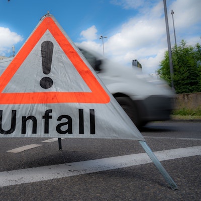 Auf einer Straße steht ein mobiles „Unfall“-Schild. Dahinter ist ein verschwommener Van.