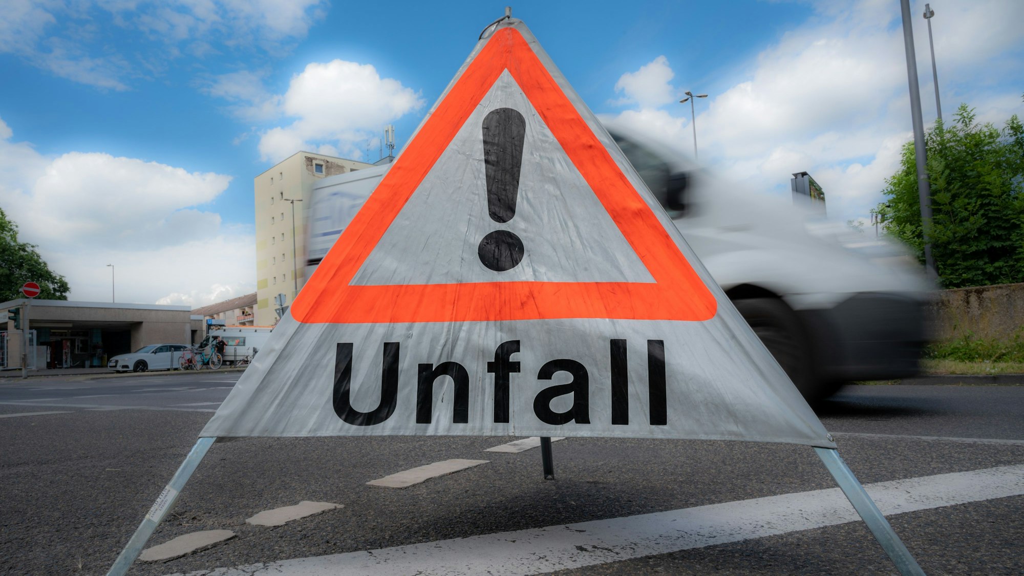 Ein mobiles Schild mit einem Warndreieck und dem Wort „Unfall“ steht an einer Straße.