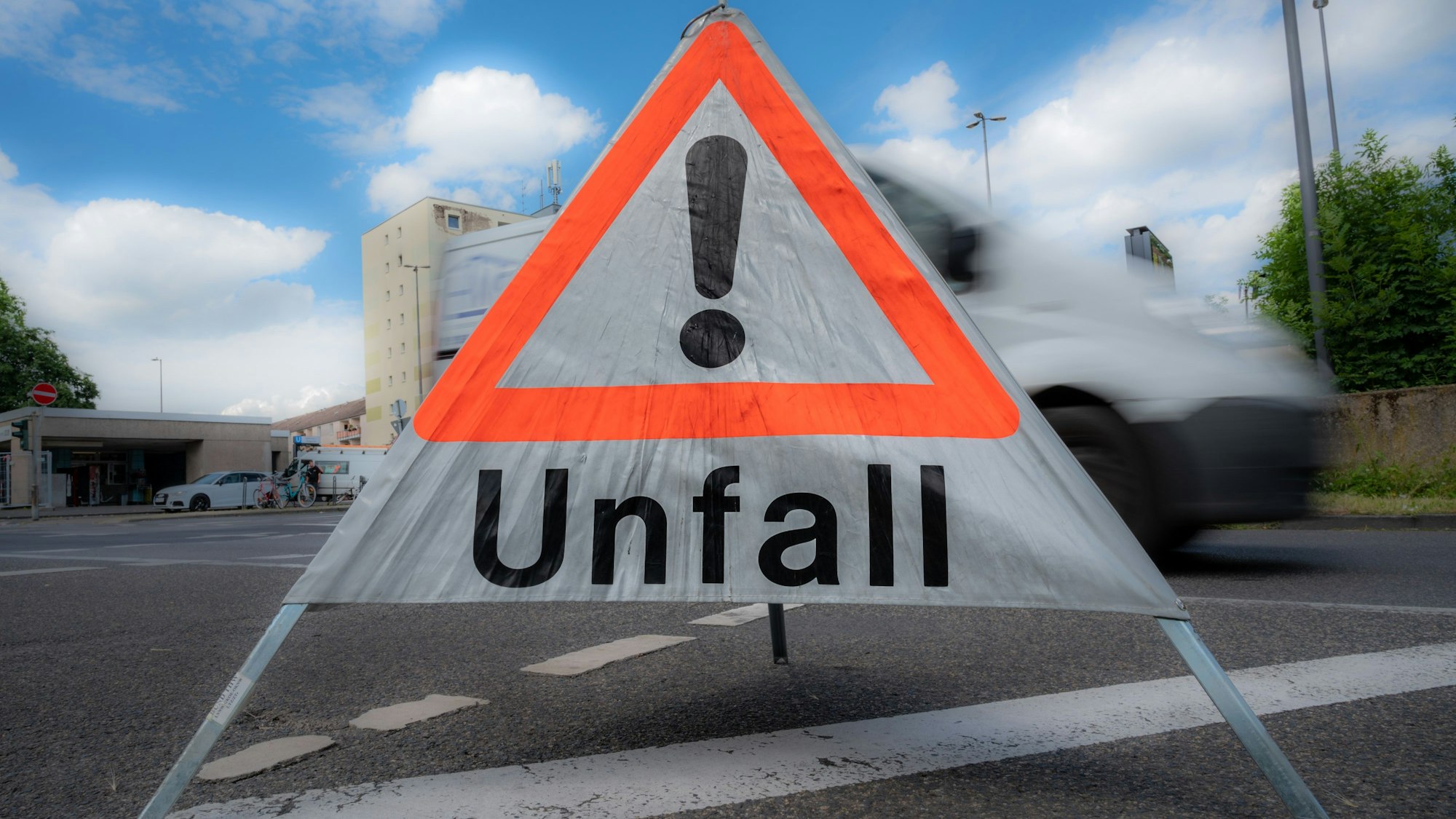 Ein mobiles Unfallschild steht auf der Straße, dahinter Autos in Bewegungsunschärfe.