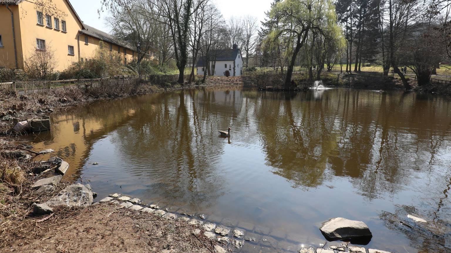 Ein Teich mit relativ niedrigem Wasserstand, im Hintergrund steht eine kleine Kapelle.