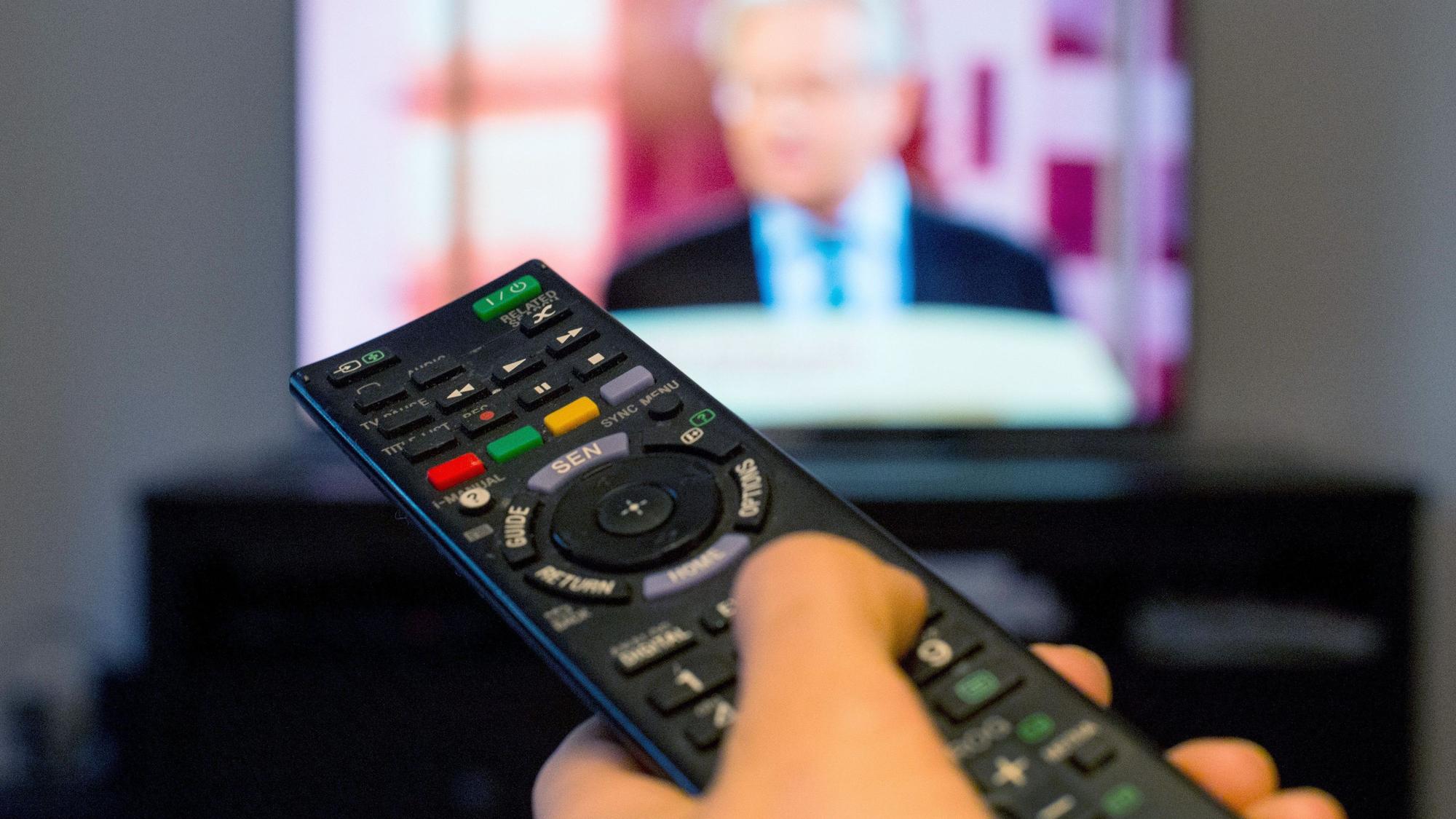 Eine Frau sitzt vor einem Fernseher und hält eine Fernbedienung in der Hand.