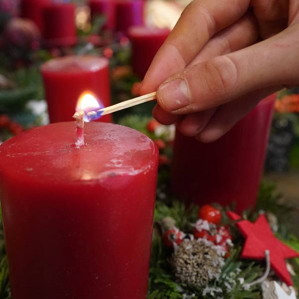 Eine Frau zündet mit einem Streichholz eine Kerze im Adventskranz an.