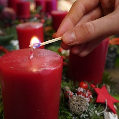 Eine Frau zündet mit einem Streichholz eine Kerze im Adventskranz an.