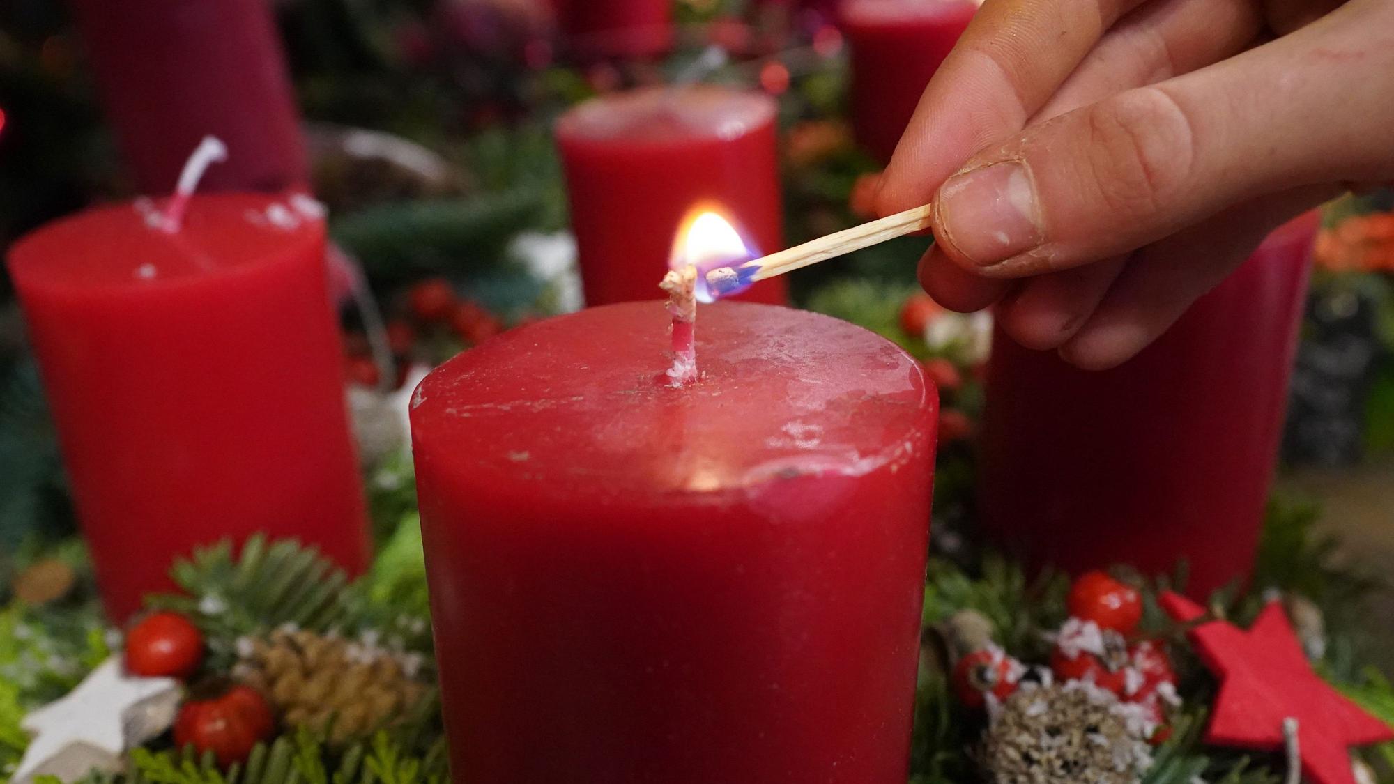 Eine Frau zündet eine Kerze eines Adventskranzes mit roten Kerzen an.