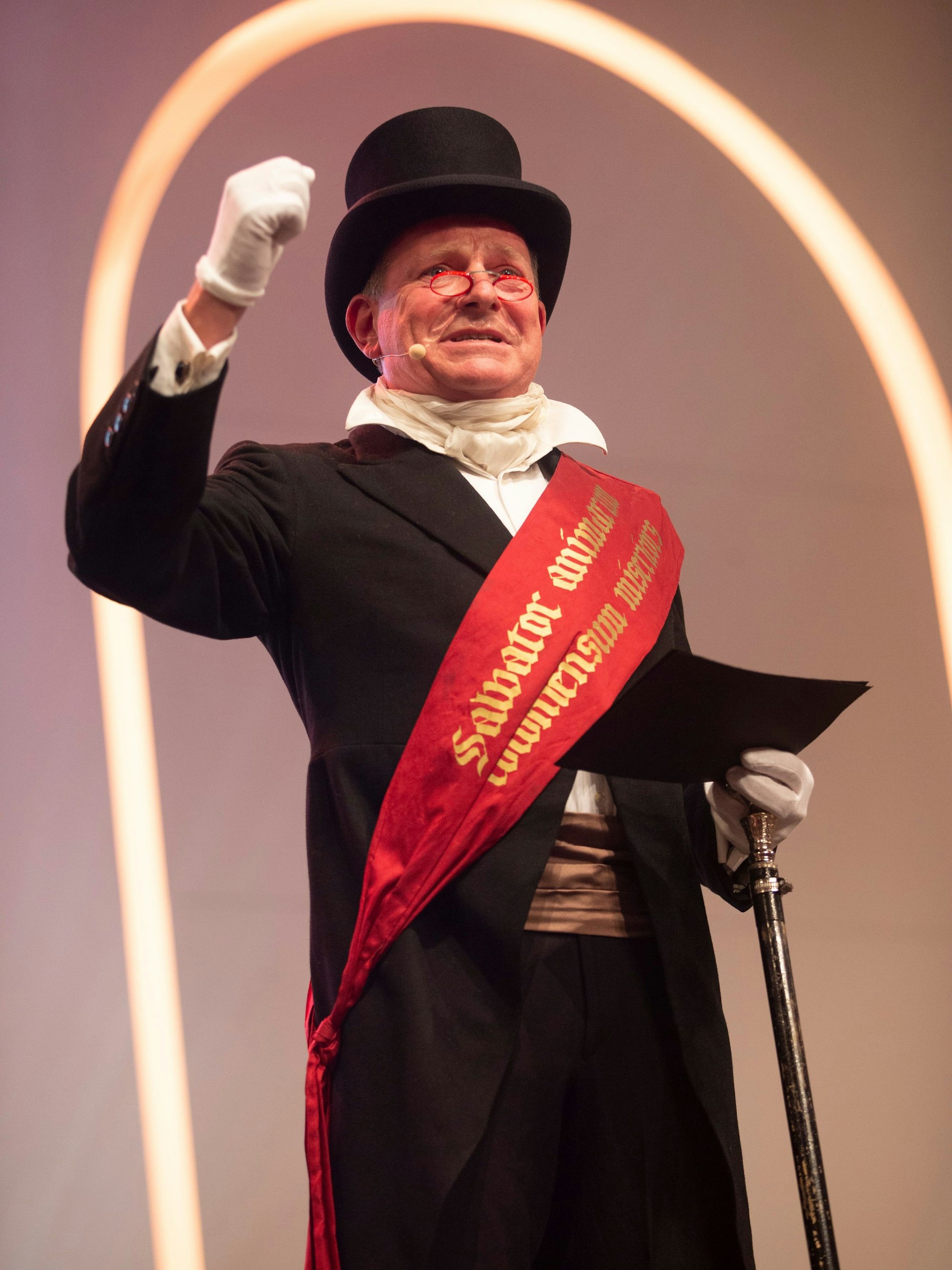 In schwarzem Anzug und mit roter Schärpe moderiert Mike Hehn als Heinrich von Wittgenstein die Veranstaltung in der Kölner Flora.