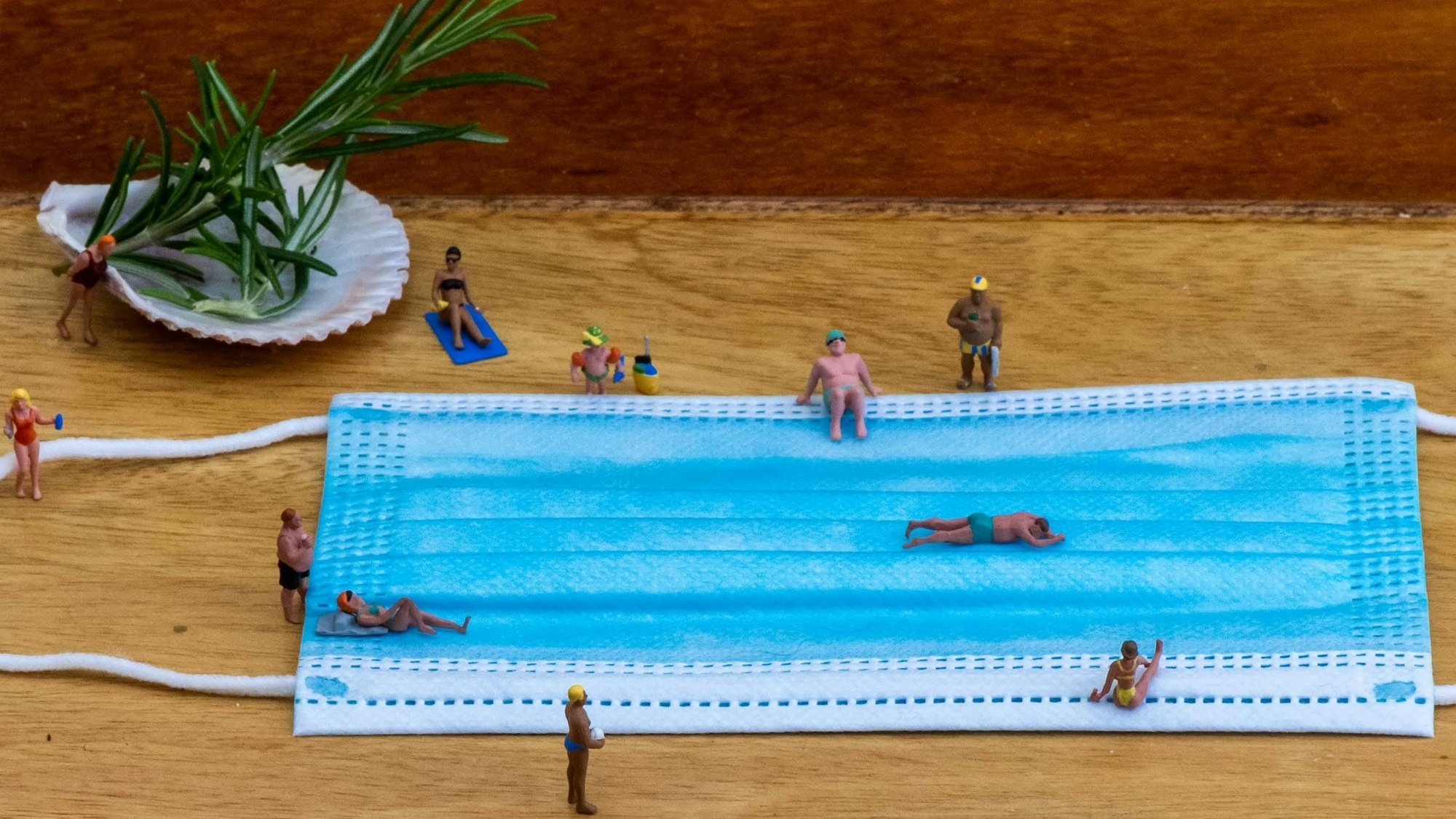 Symbolisch bewegen sich Püppchen um eine Corona-Schutzmaske wie in einem Bad.