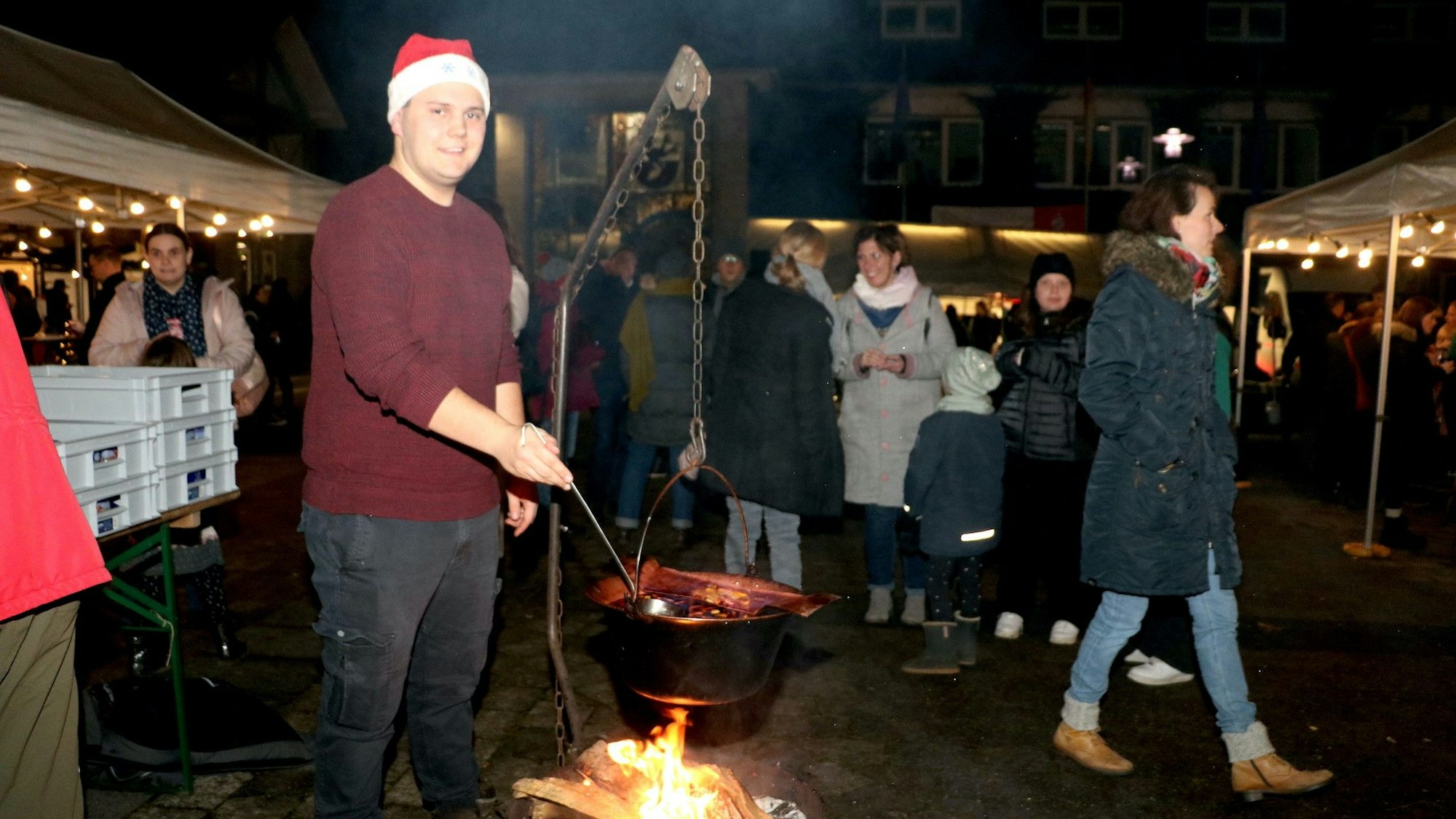 Ein junger Mann mit Nikolausmütze rührt mit einer Kelle in einem Kessel auf dem Kürtener Weihnachtsmarkt.