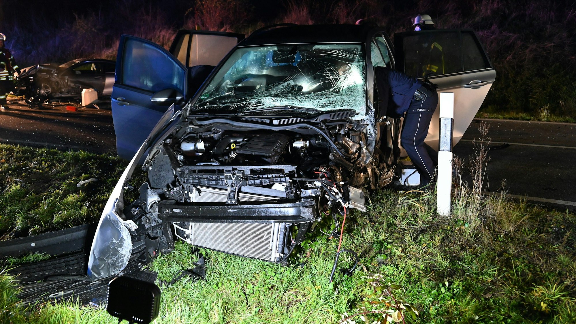 Ein fast vollständig zerstörter Pkw nach dem Unfall auf der K16 in Kerpen. Polizisten untersuchen das beschädigte Auto.