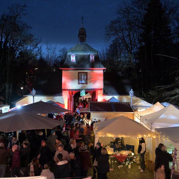 Ein Blick von oben auf den Weihnachtsmarkt an Schloss Eulenbroich in Rösrath. Besucher stehen an den zahlreichen, weißen Ständen. Im Hintergrund ist das angestrahlten Tor zum Schlossgelände zu sehen.