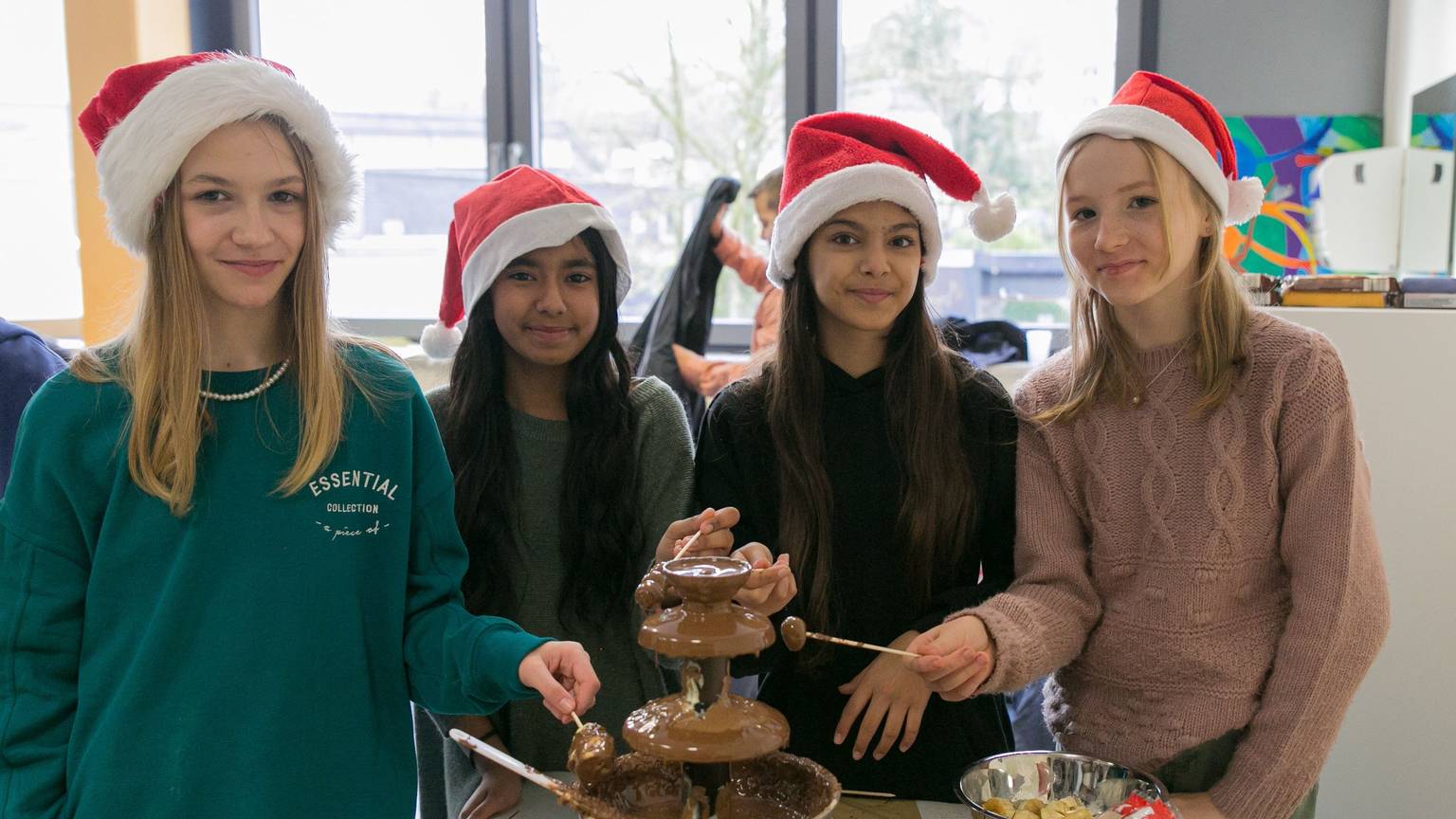Lea, Riam, Anastasija und Isa tragen Nikolausmützen auf dem Kopf und halten Früchte in einen Schokoladenbrunnen.