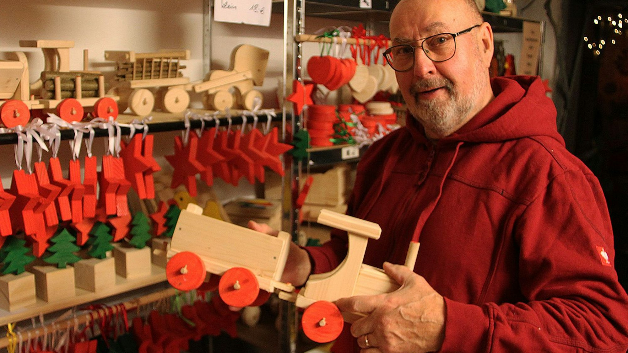 Alt-Ortsbürgermeister Reinhold Rader hält eine selbst geschnitzte Holzeisenbahn in der Hand. Im Hintergrund ein Regal mit weiterem Holzspielzeug.