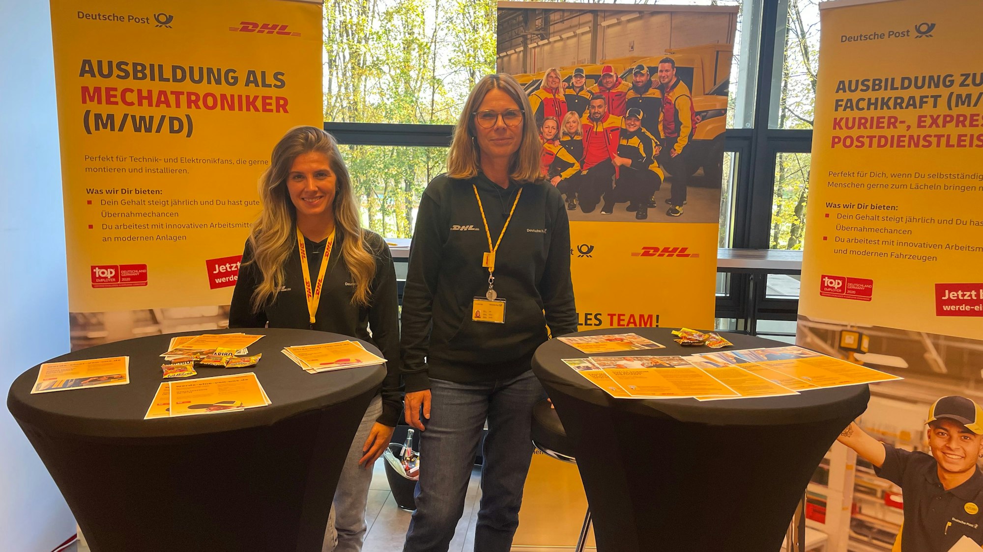Ela Tuna und Simone Tolk von DHL stehen nebeneinander an zwei Stehtischen auf dem Karrieretag.