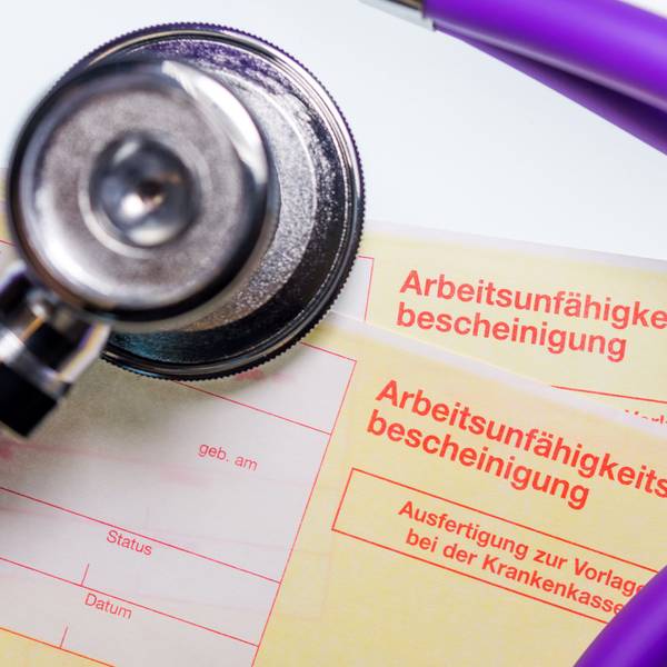 Eine Arbeitsunfähigkeitsbescheinigung und ein Stethoskop liegen auf einem Tisch.