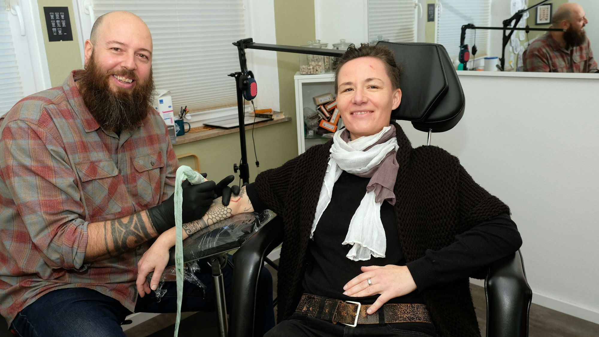 Im Tätowierstuhl im Studio „4 Monkeys“ in Gemünd hat Tätowiererin Manu Platz genommen, während ihr Kollege Peter die Tätowiernadel ansetzt.