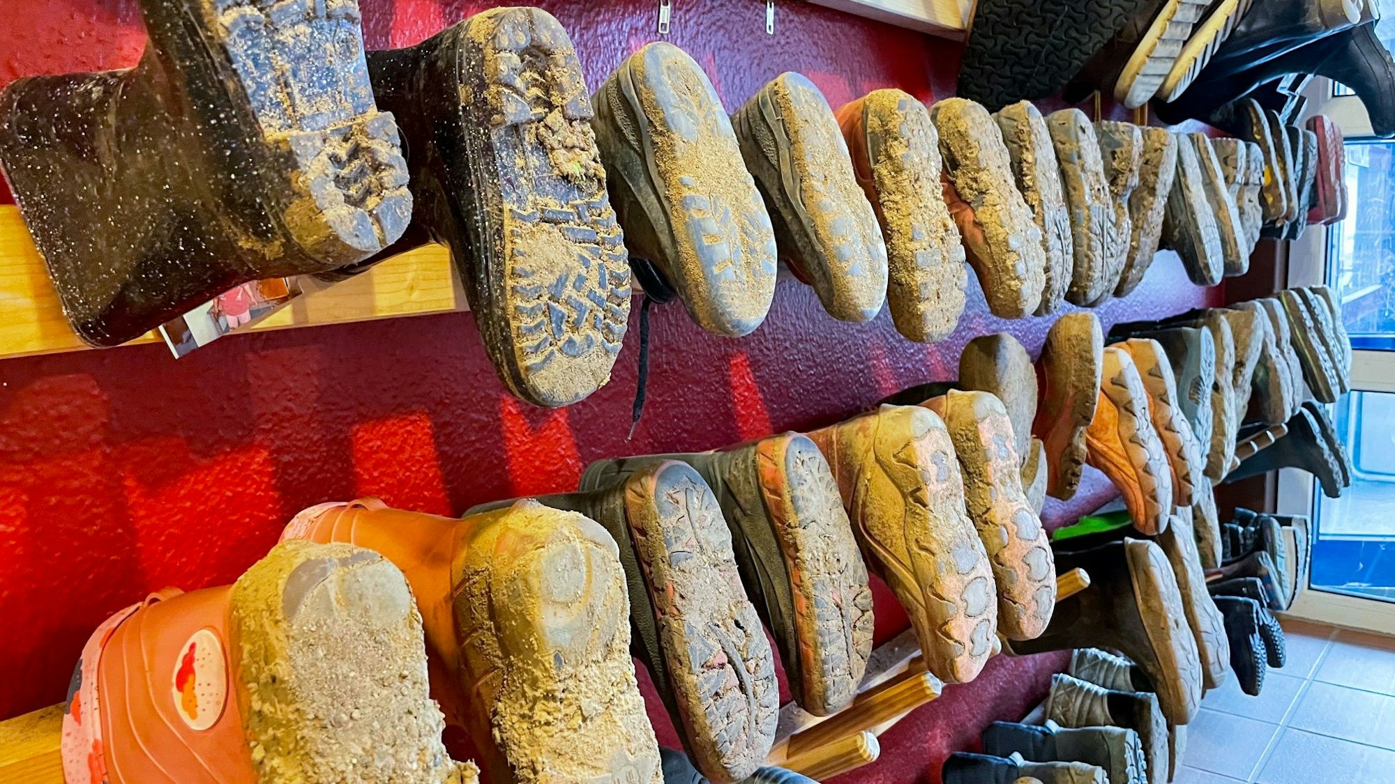 Dreckige Gummistiefel hängen in einem Kindergarten.