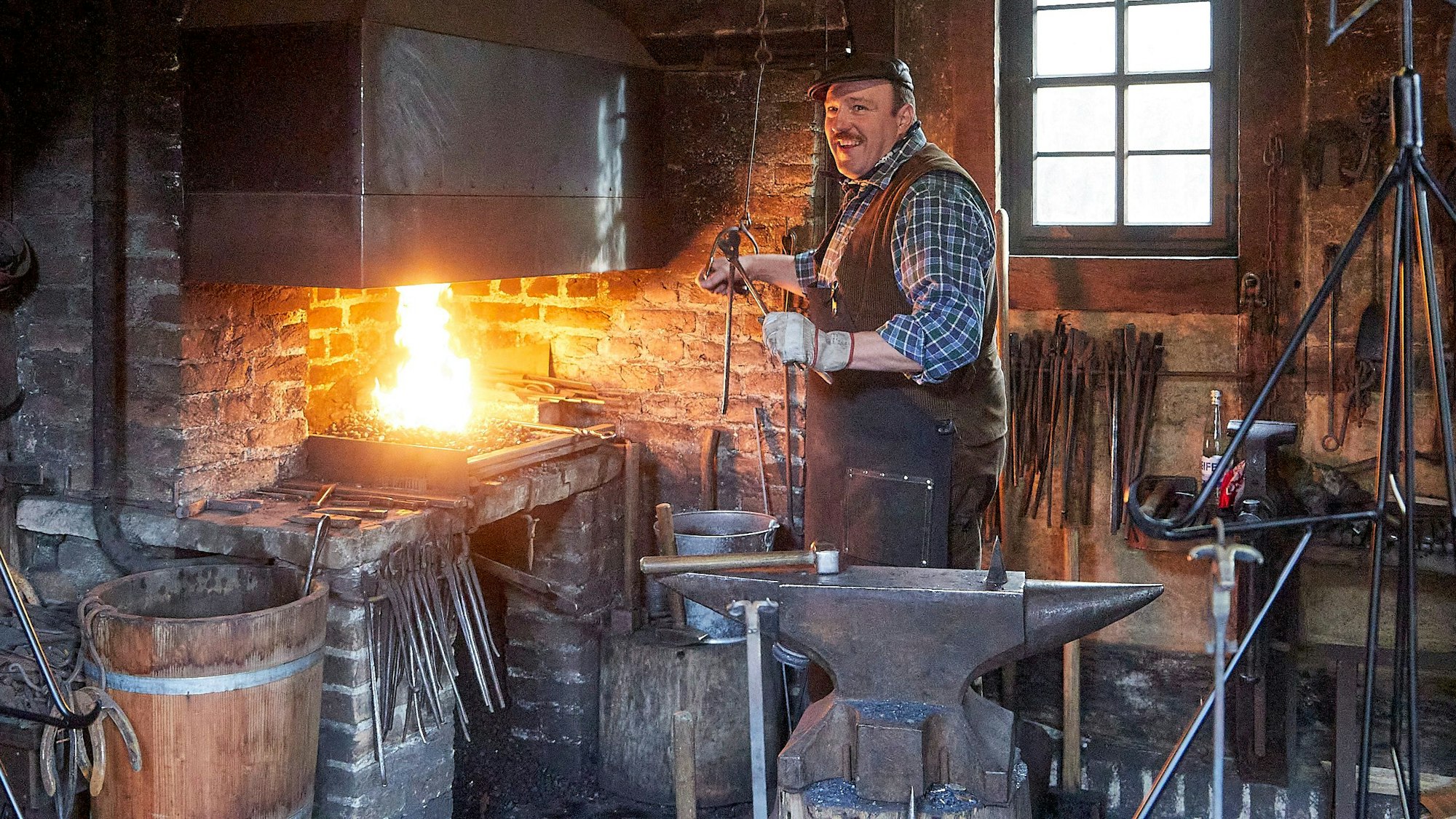 Museumsschmied Dieter Knoll steht in seiner Schmiede mit den zahlreichen Werkzeugen im Kommerner Freilichtmuseum am Amboss. Das Feuer lodert.