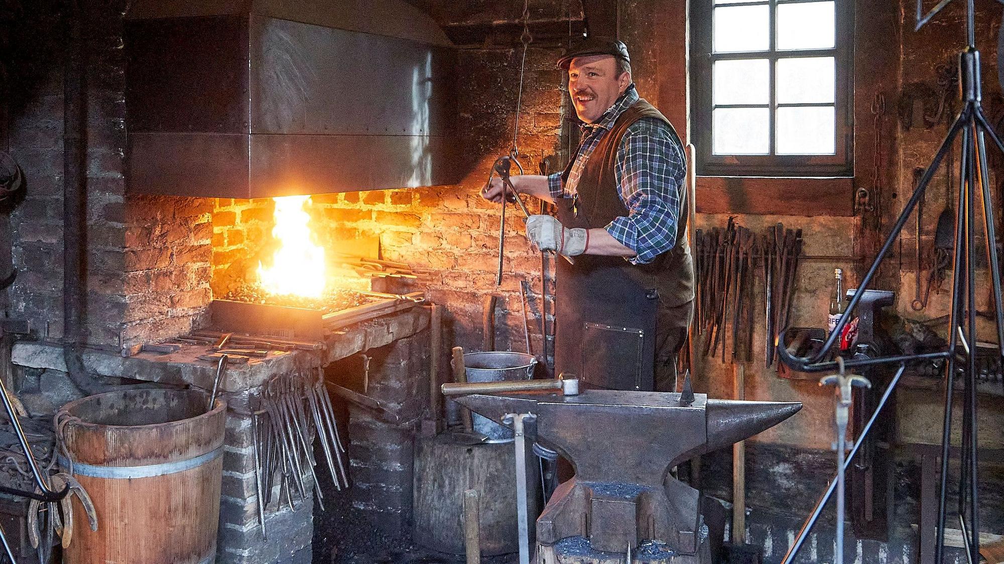 Museumsschmied Dieter Knoll steht in seiner Schmiede mit den zahlreichen Werkzeugen im Kommerner Freilichtmuseum am Amboss. Das Feuer lodert.