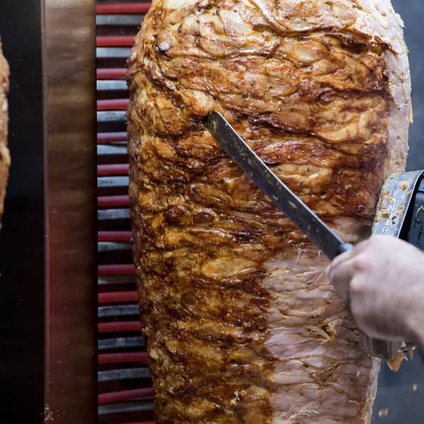 Jemand schneidet Fleisch mit einem elektrischen Gerät von einem Dönerspieß.