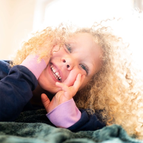 Ein Kind liegt auf einer Decke im Kindergarten und lächelt.