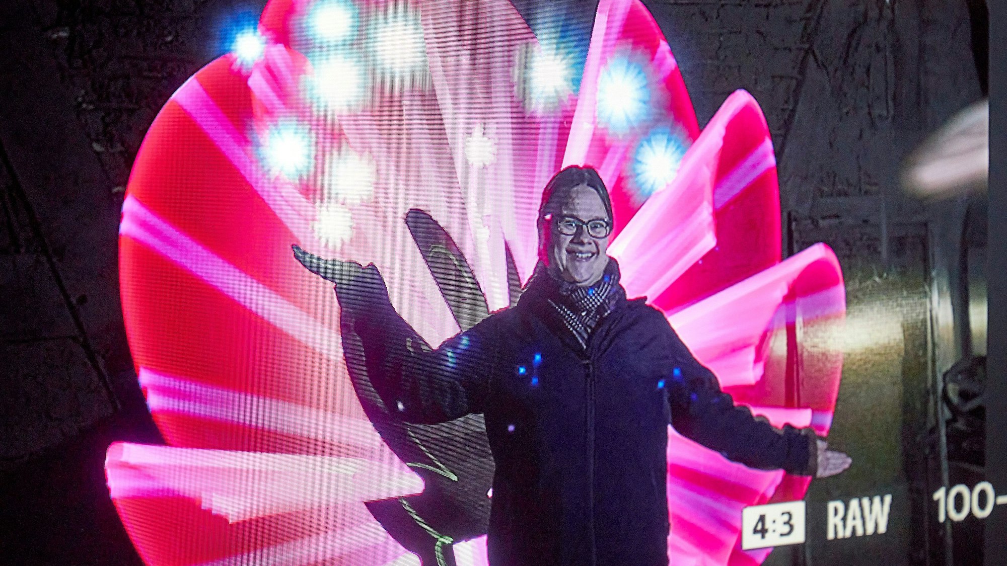 Eine Frau steht vor einer Fotowand und gestikuliert.