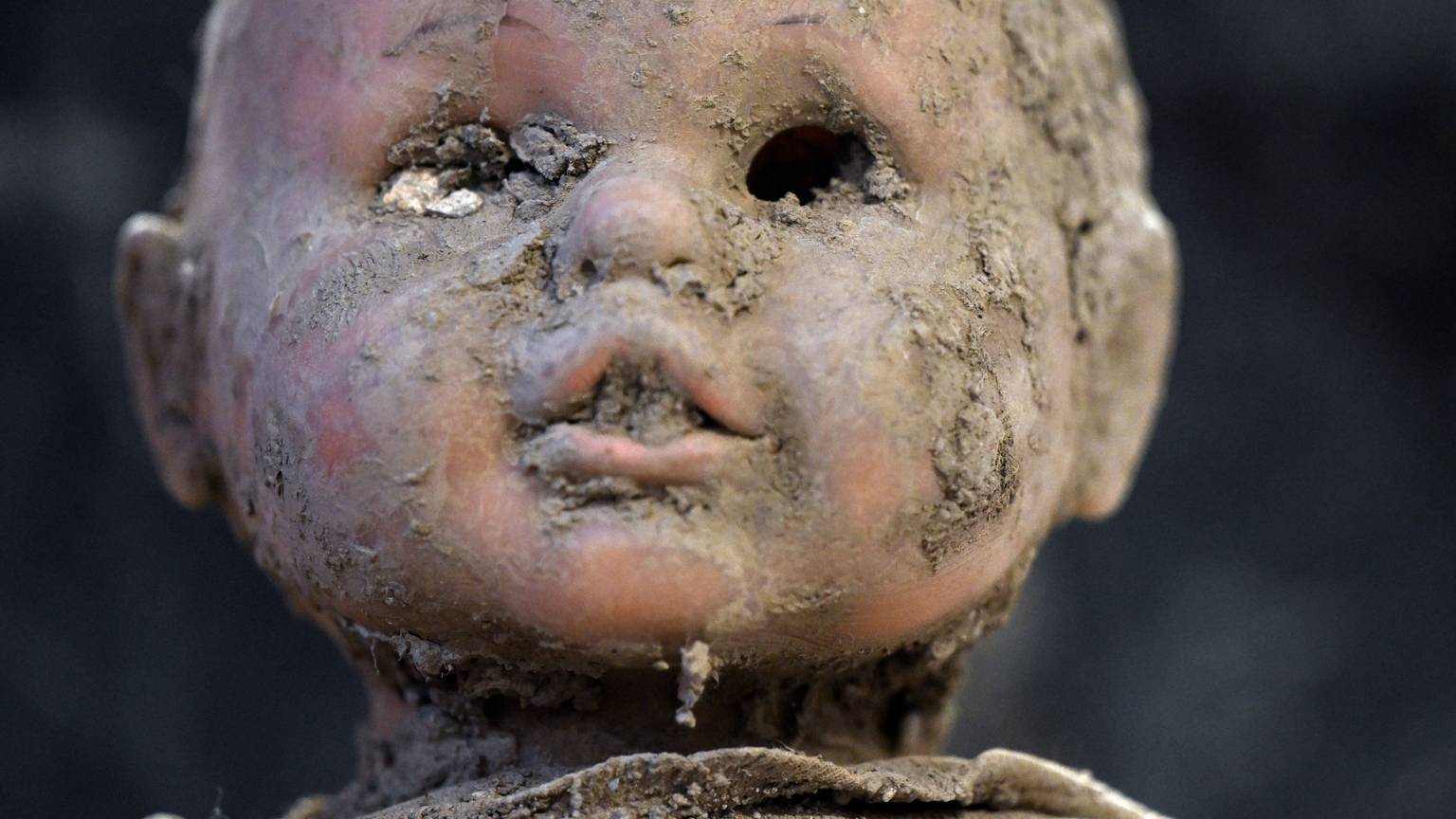 Der Kopf einer Puppe ist verschlammt, im Mund steckt Dreck, die Augen fehlen.